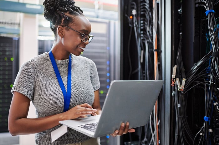 A person with a laptop looking at servers in a data center. 