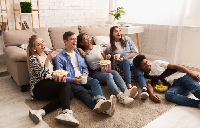 A group of young friends sitting on the floor watching television.