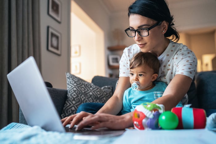 Parent holding child on lap and typing on laptop.