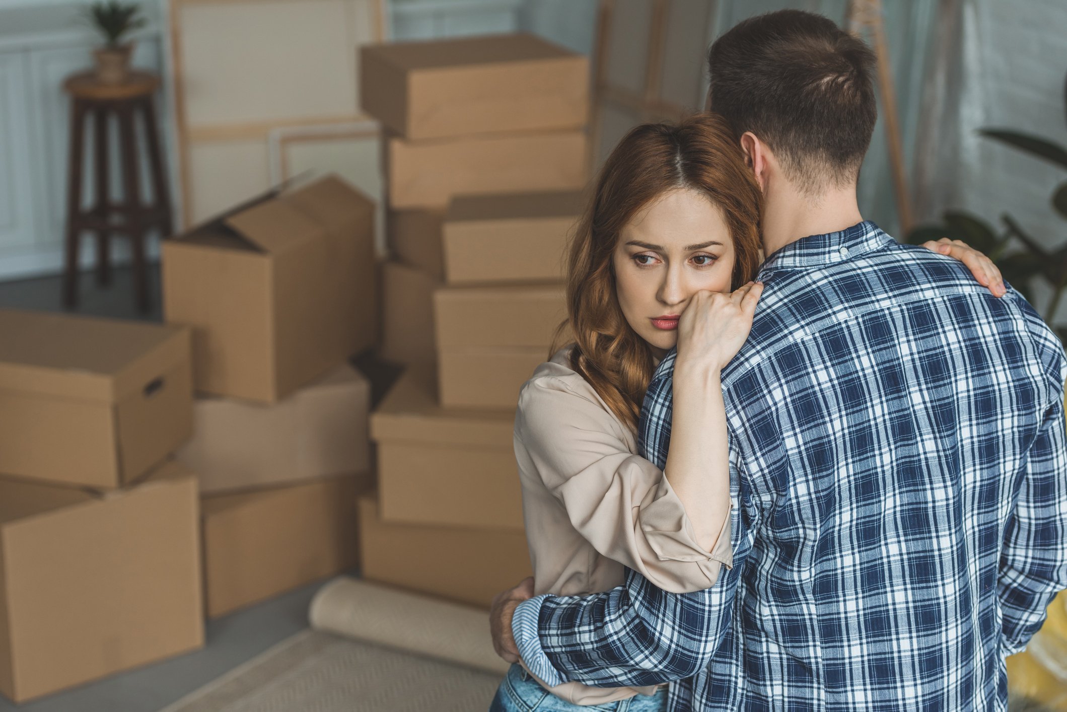 Person looking sad while hugging partner in room full of moving boxes