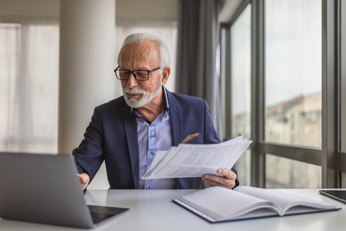 A person at a laptop holding documents.