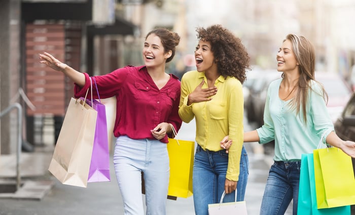 Teens with shopping bags walking on a street.