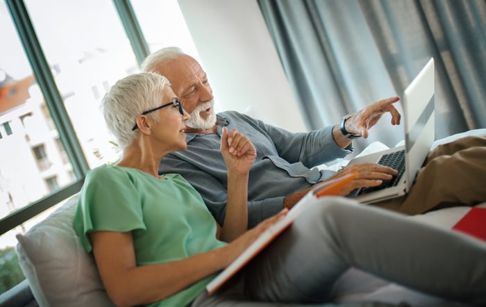Two people sitting on a sofa while looking at a laptop.