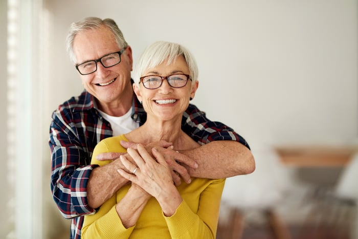 A couple is indoors, one hugging the other, and smiling. 