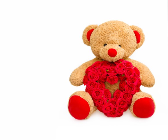 A stuffed teddy bear with roses in the shape of a heart.