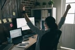 Person celebrating while looking at two computer screens with stock charts