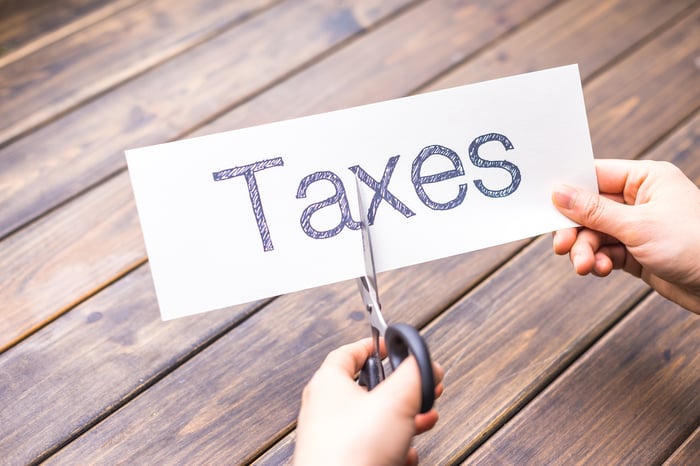 A person cutting a piece of paper with the word Taxes printed on it.