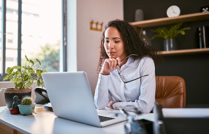 A person at a laptop holding a pair of eyeglasses.