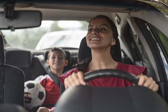 A person driving a child with a soccer ball in a car.