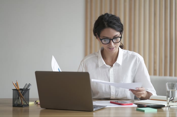 A person sitting at a desk reviewing documents in front of a computer monitor.