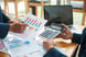 22_04_25 Two people comparing charts with a calculator and computer on a table _GettyImages-1212963371