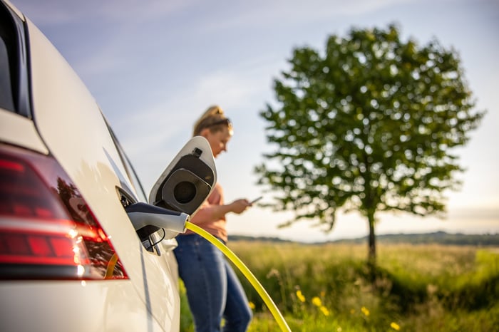 Woman charges her electric vehicle next to a tree while on her cell phone.