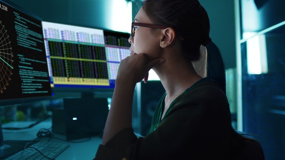 Person sitting at a computer and looking at monitors with stock prices and charts.