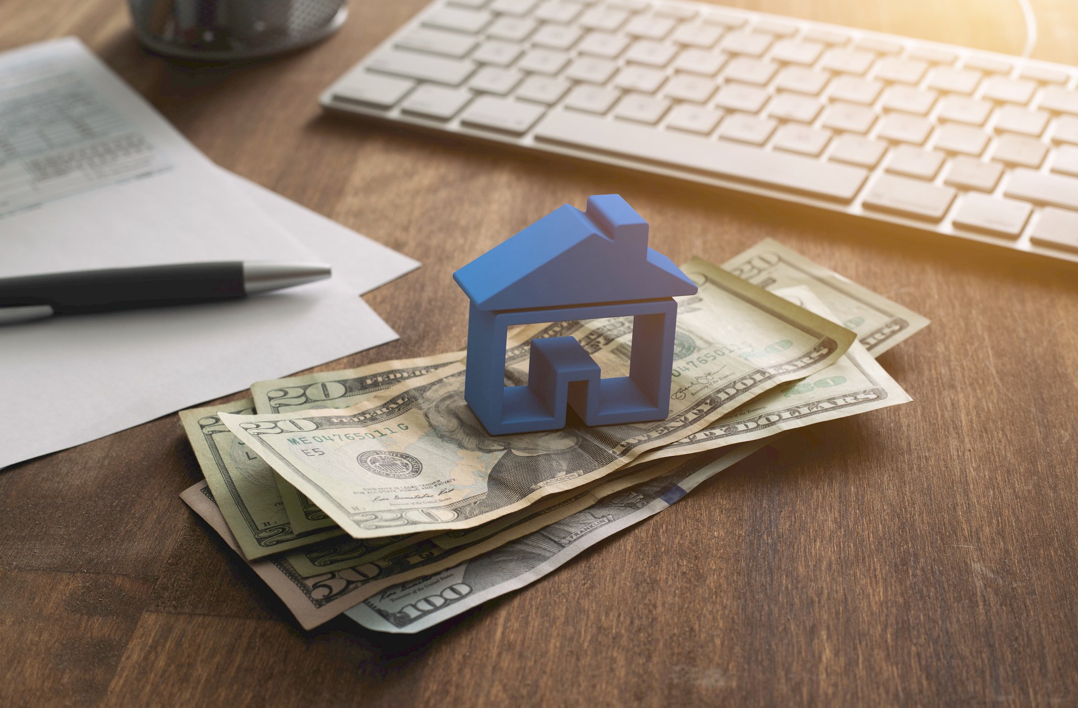 A house paperweight atop a stack of dollar bills on a desk