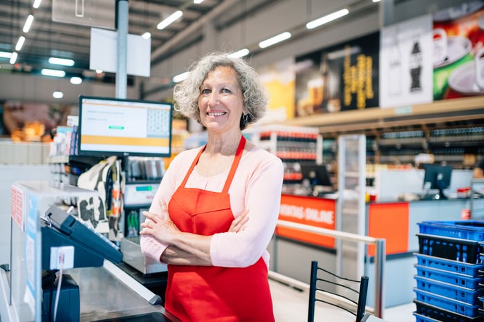 A smiling person in an apron at a register.