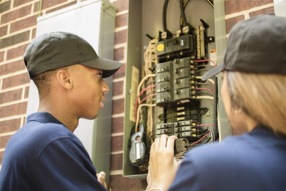 Two people working with an electric power box.