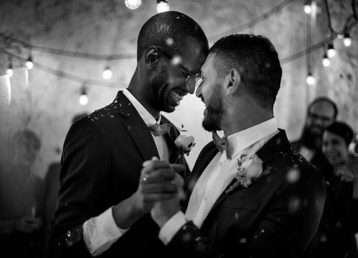 A couple, in black and white, are smiling and dancing at their wedding.