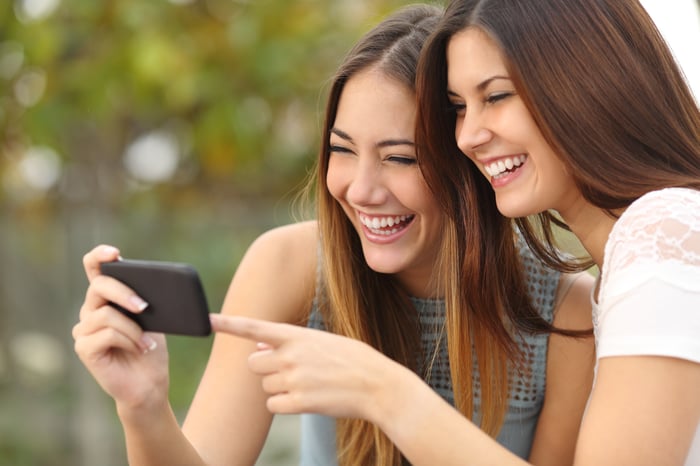 Two people laughing while watching a video on a smartphone.