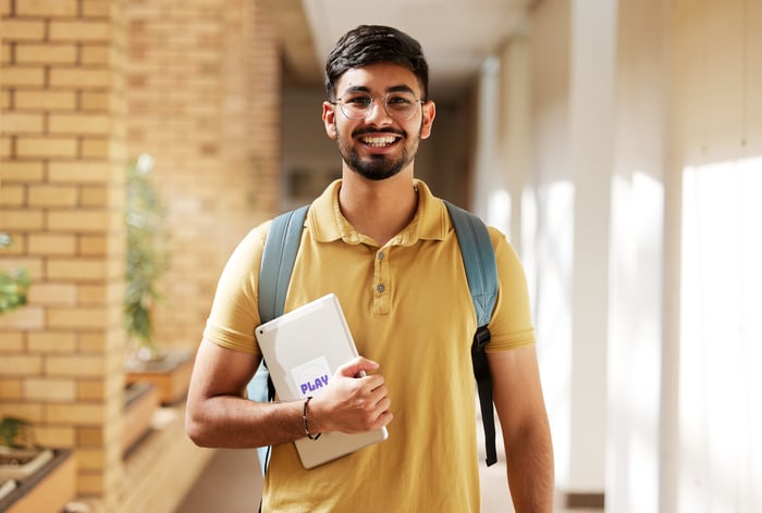 A smiling person wearing a backpack and holding a tablet.