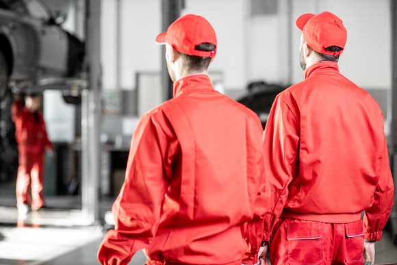 Two people in bright red uniforms in an auto shop.