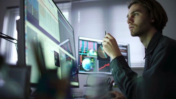 A person looking at charts and graph across multiple computer monitors.
