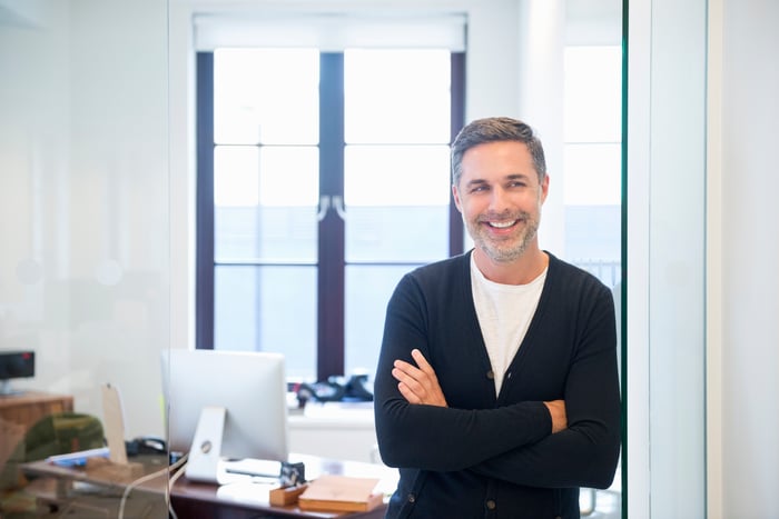 A smiling person in front of a desk.