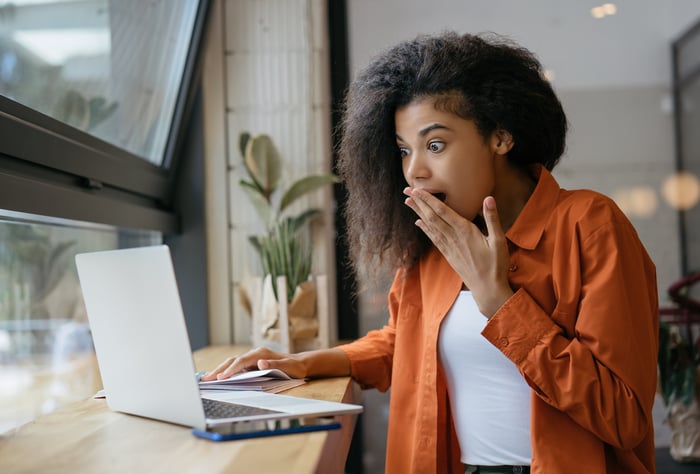 A surprised person holding hand to mouth while looking at a laptop PC.