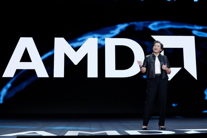 AMD CEO Lisa Su speaking in front of large AMD logo.