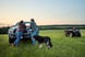 Two people lean against a pickup truck in a farm field.