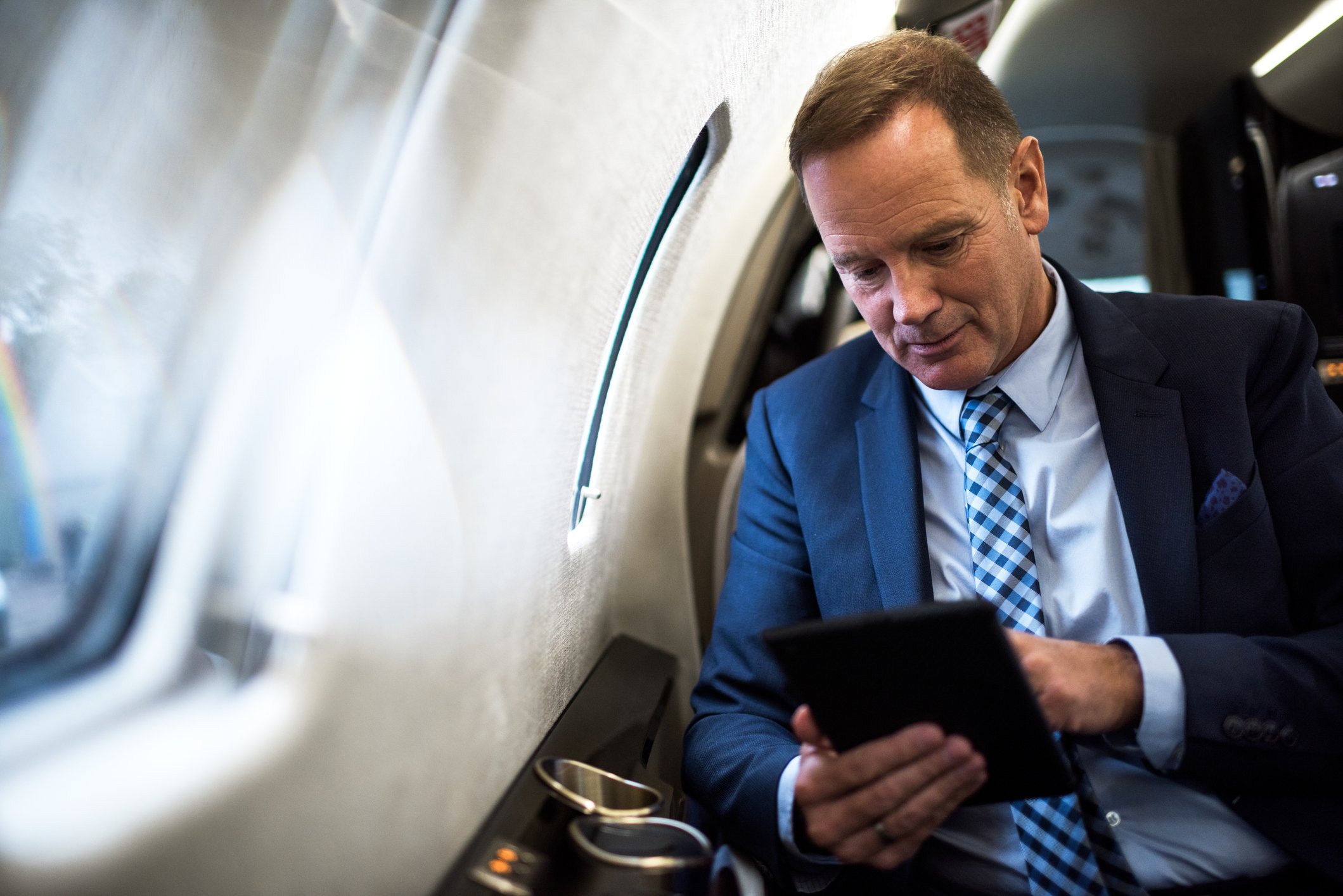 investor smiles while looking at tablet in airplane