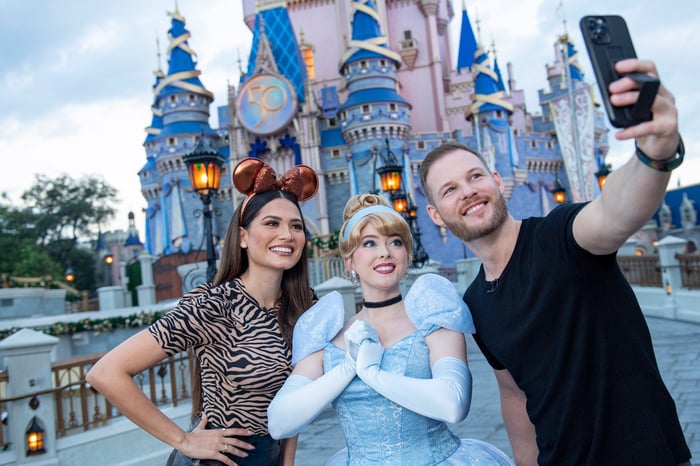A Disney Princess and park guests take a selfie in front of the Magic Kingdom castle.