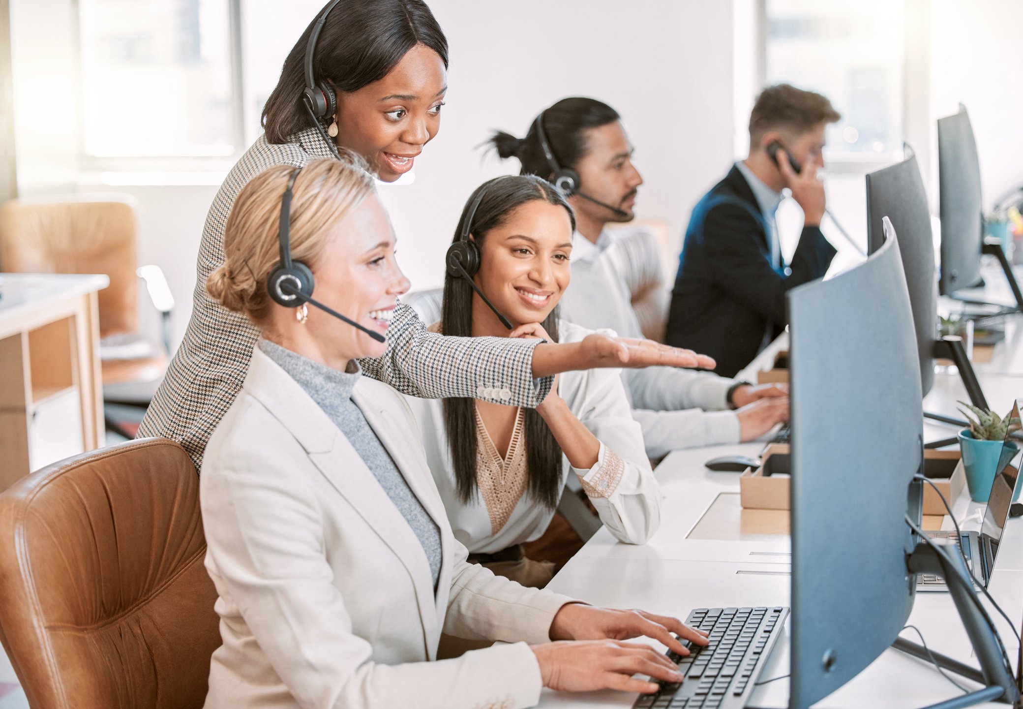 call center agents wearing headsets and working together on a computer in the office