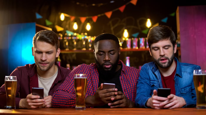 Three men sitting a bar, looking at their phones.