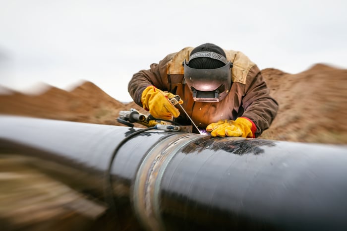 A person in protective gear welding an energy pipeline.