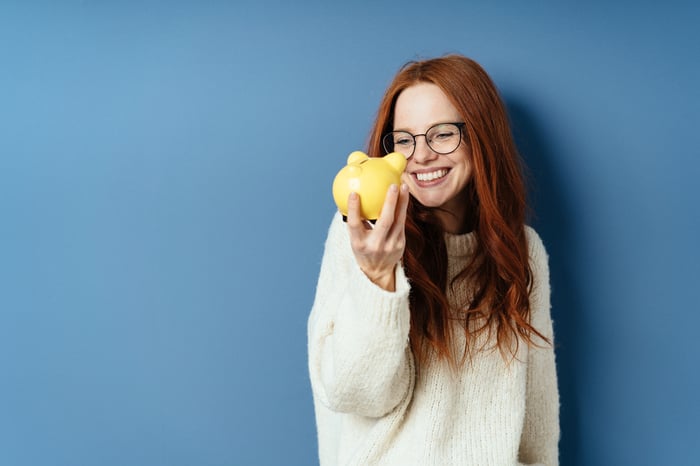 Someone smiling and holding a piggy bank in hand.