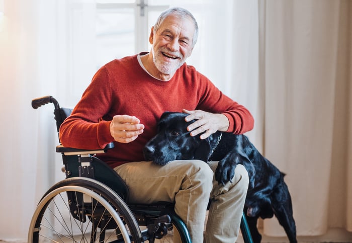 Person in wheelchair smiling and petting a dog.