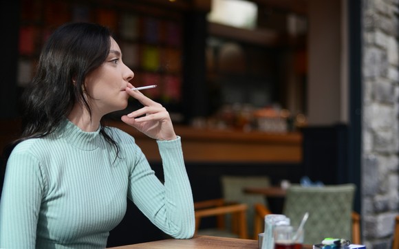 A person smokes a cigarette while seated at a table.