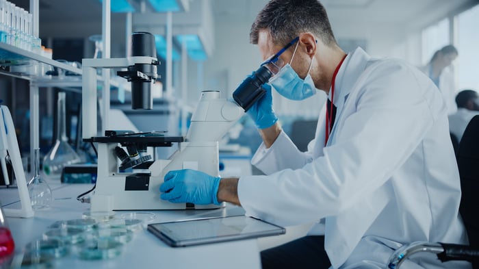 A scientist looks into a microscope while sitting at a lab bench.