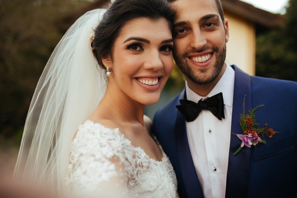 A couple in wedding attire is smiling at the camera.