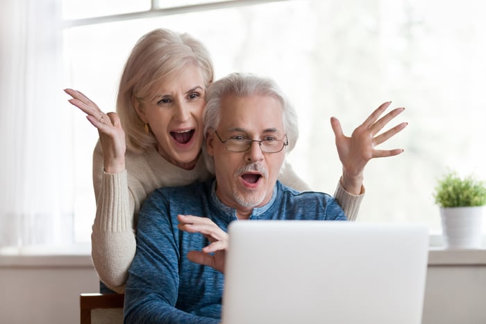 A couple is looking at a laptop screen and smiling in surprise.