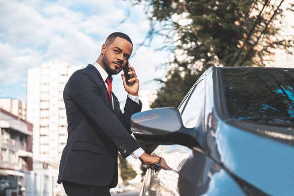 Someone holding a mobile phone while going into a car.