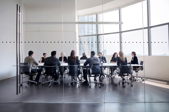 Professionally dressed executives having a meeting around a table in a glass-walled conference room.