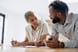 Two people leaning forward on desk, talking.