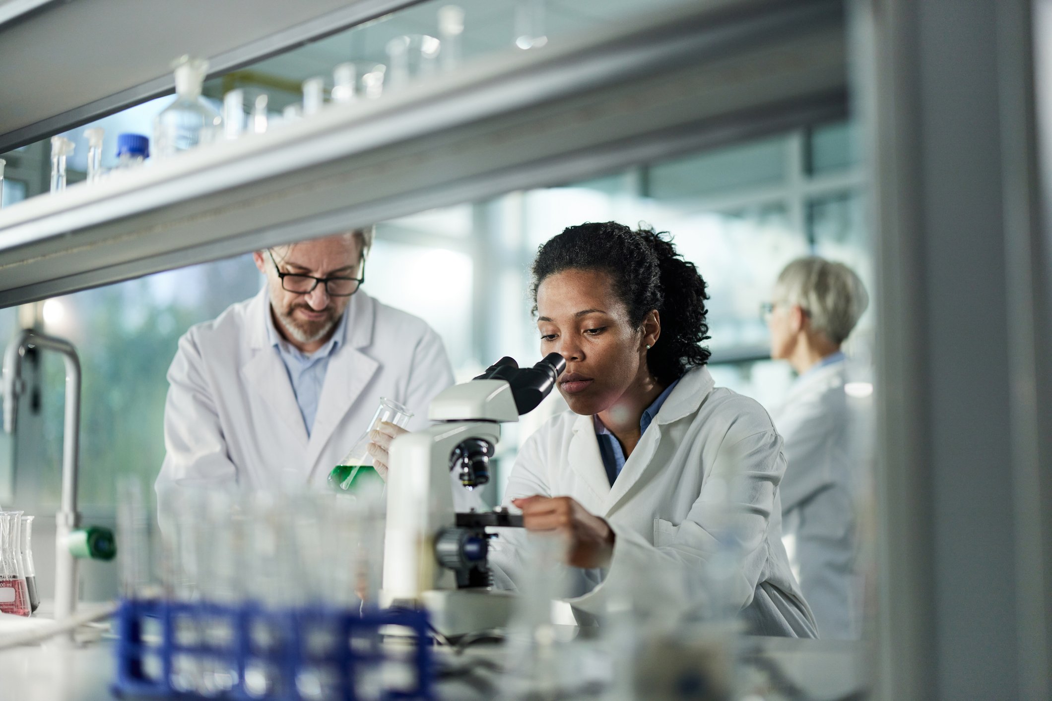 three scientists work in laboratory with one looking down a microscope