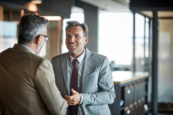 Two people in business attire standing and talking.