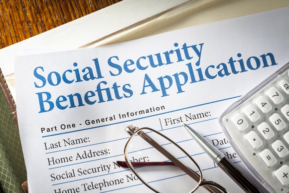 A pair of glasses, a pen, and a calculator, set atop a Social Security benefits application.
