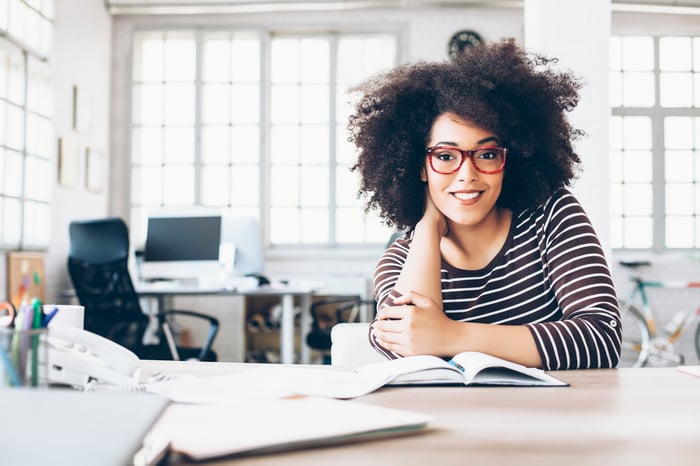 A smiling person with an open book in front of them.