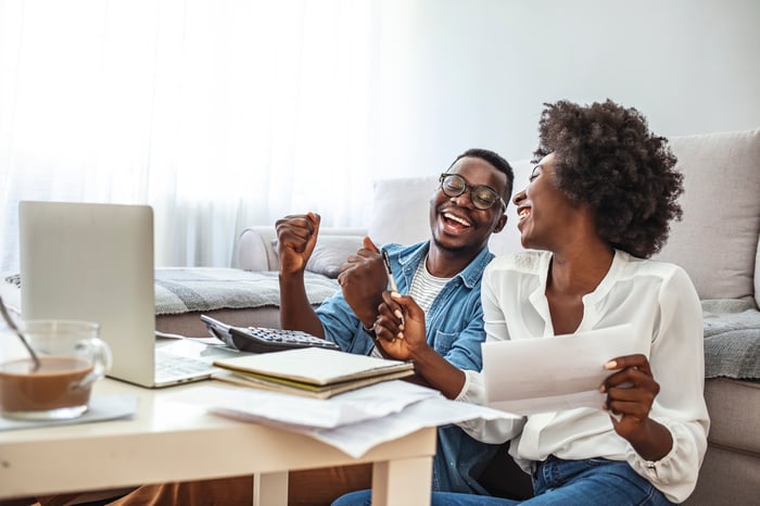 Two people laughing in front of a laptop and paperwork.