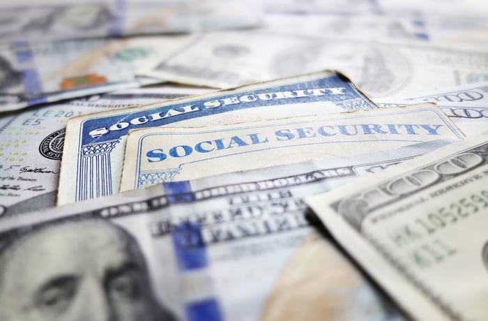 Two Social Security cards surrounded by a messy pile of one-hundred-dollar bills.