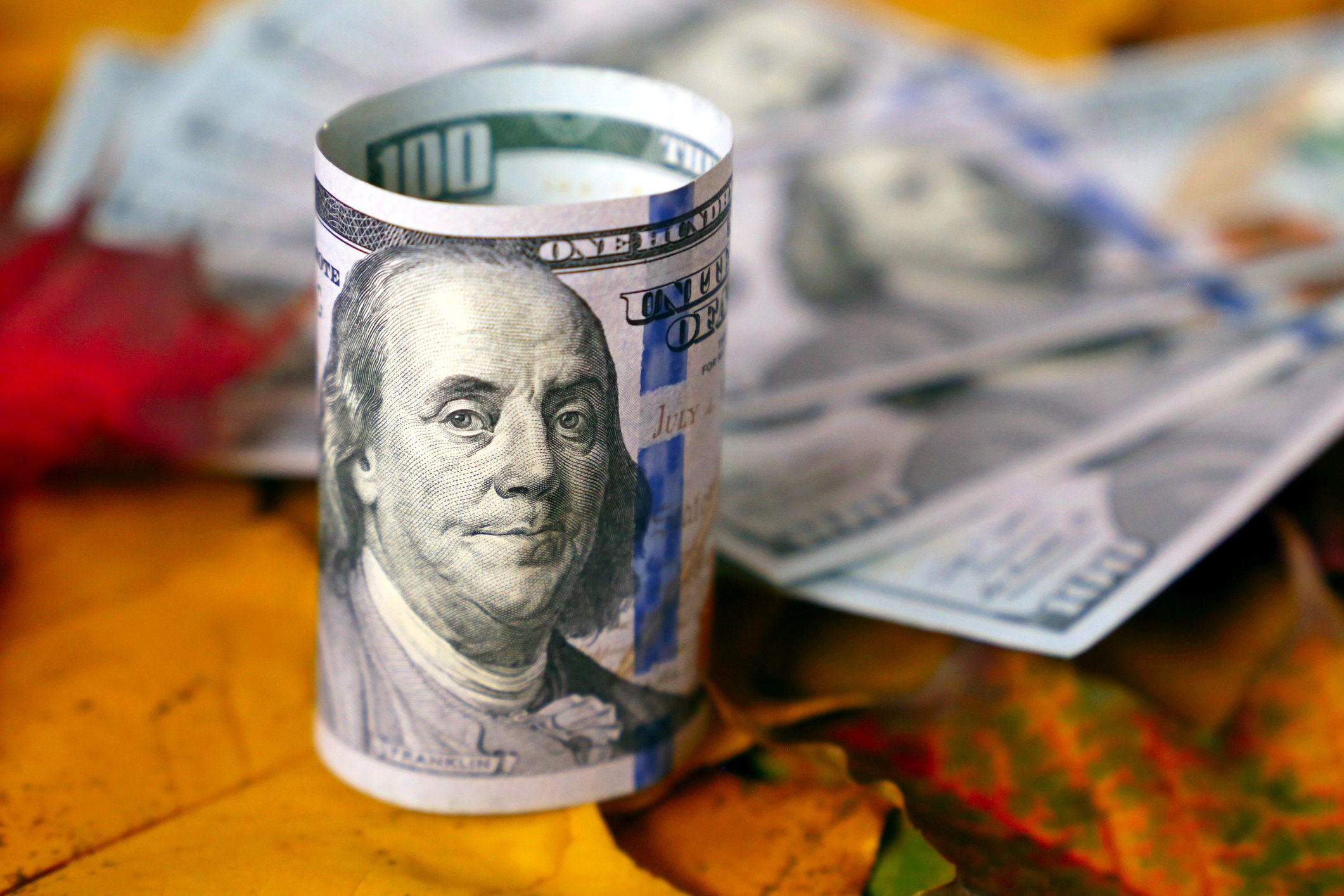 Roll of hundred-dollar bills on autumn maple leaves